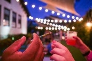 hand holding cannabis joint with lights and garden in background